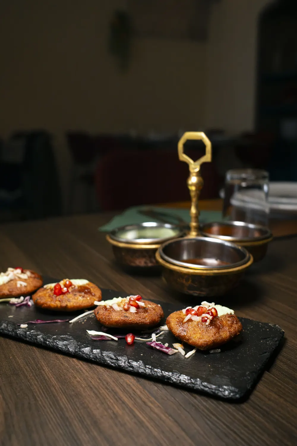 Aloo Tikki sulla lavagna e il portasalse in ottone, con la sala sullo sfondo