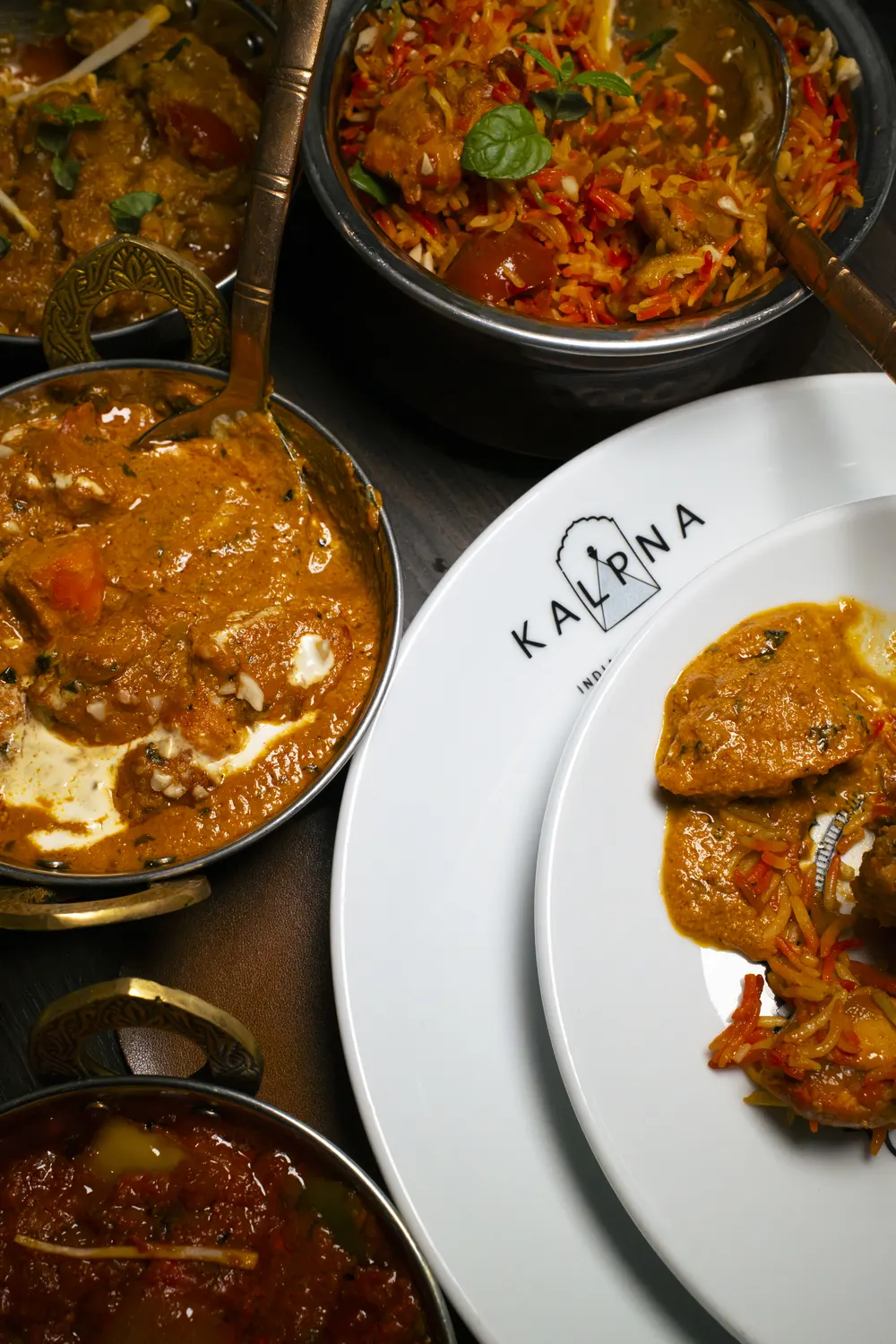 Tavola con biryani, curry e il piatto col logo Kalpna