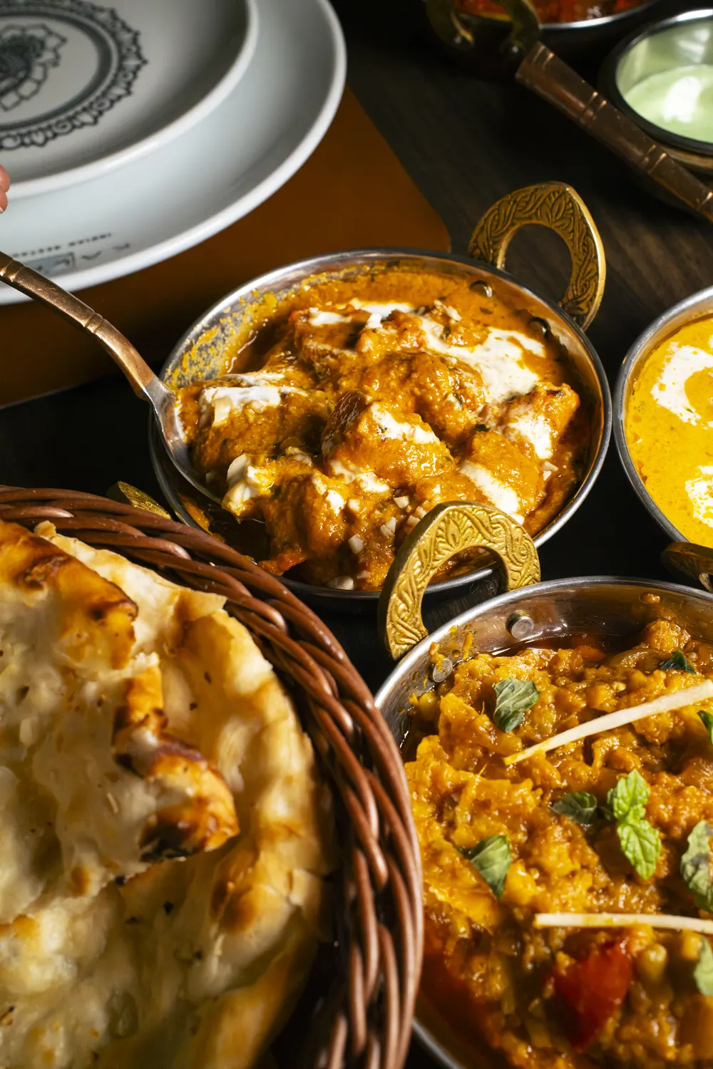 Curry nelle ciotole in rame accanto a un cesto di naan