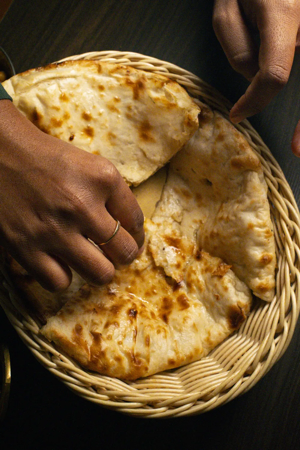 Mani che spezzano un naan appena uscito dal tandoor