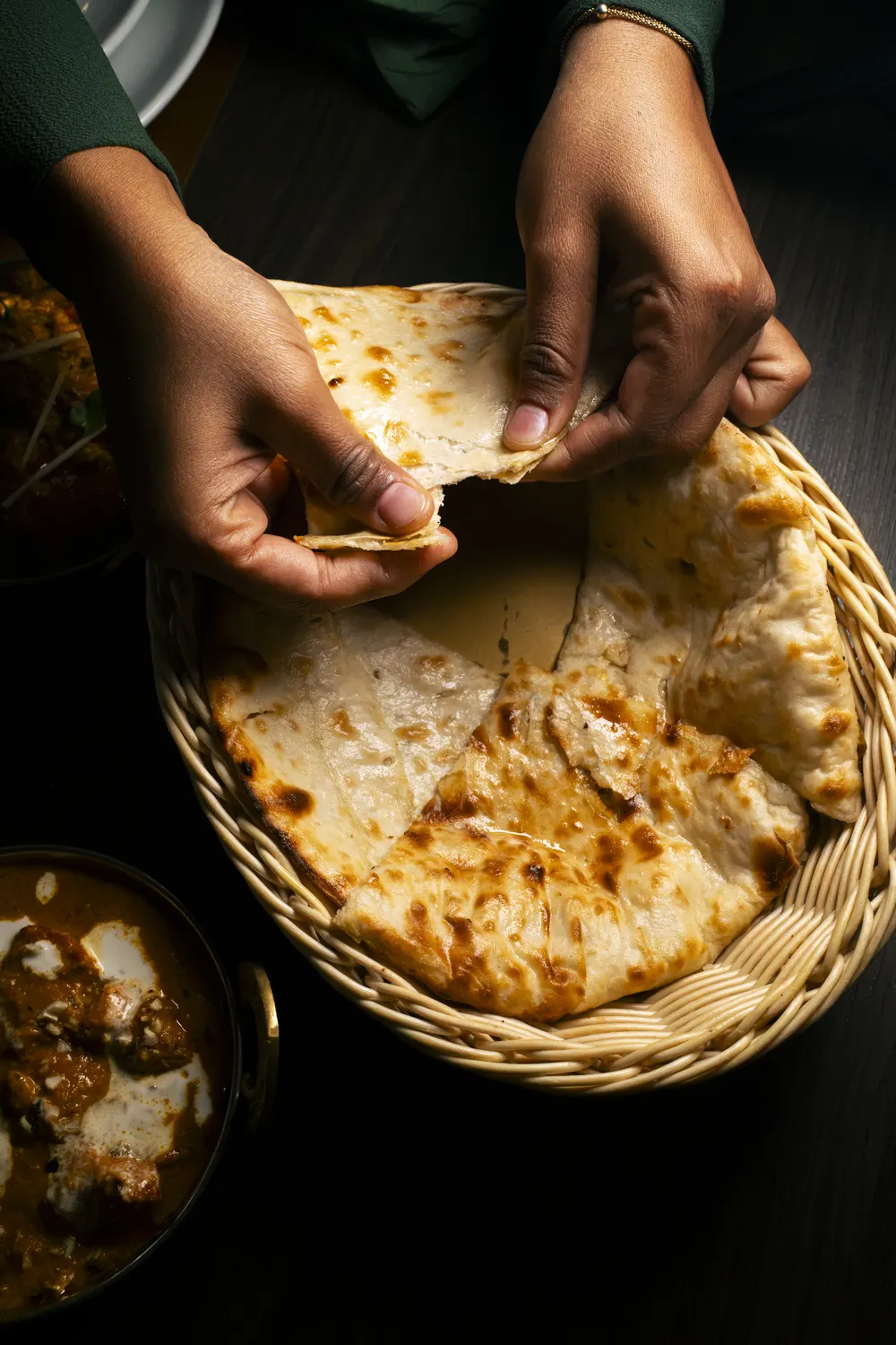Due mani che spezzano un naan nel cesto di vimini
